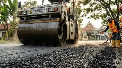 Mesin road roller memadatkan hamparan aspal sementara pekerja merapikan permukaan jalan