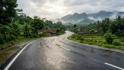 Jalan aspal yang baru selesai dikerjakan terlihat basah setelah hujan dengan pemandangan perbukitan di kejauhan.